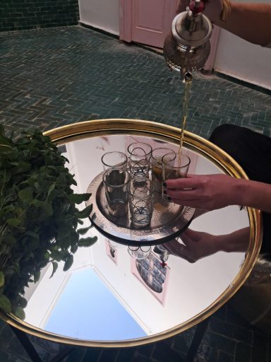 Main en train de verser du thé dans des verres sur une table réfléchissante.