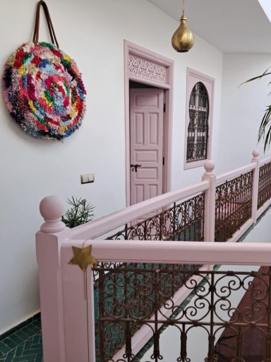 Couloir décoré avec un mur rose, une porte et un tapis mural coloré.